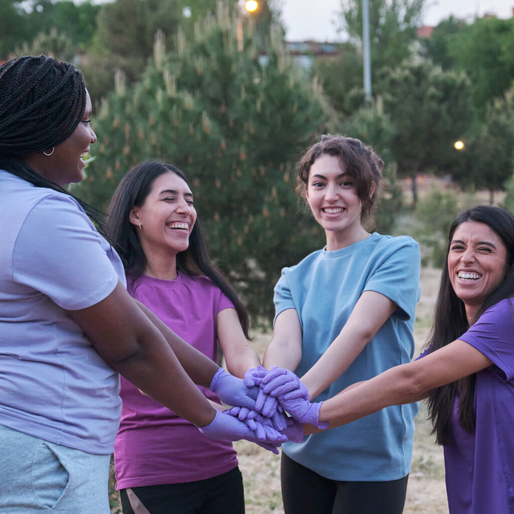 Group of multiracial active women smiling and putting their hands together after picking up trash in nature. Plogging concept.